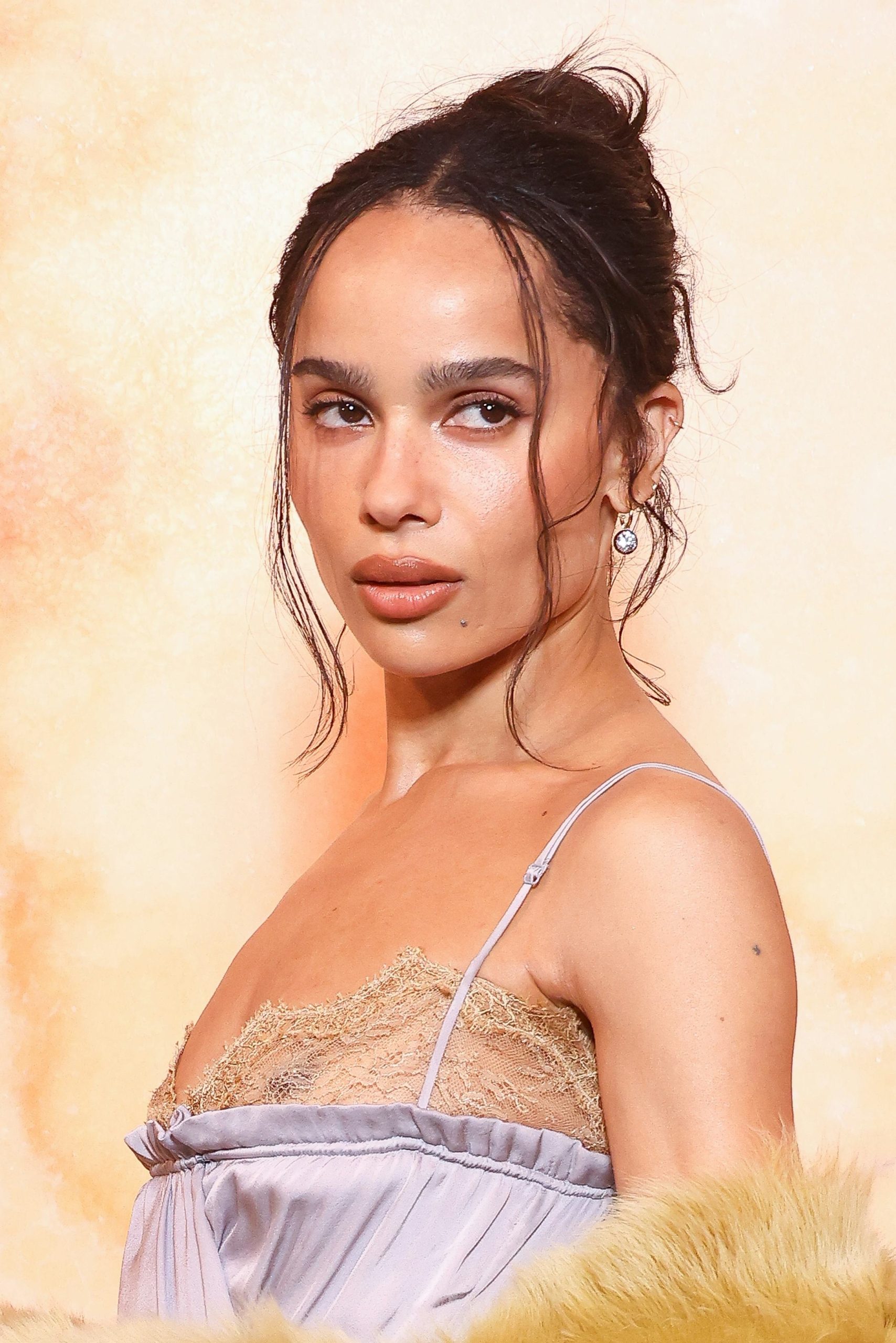 Woman with dark hair in an updo wearing a lavender dress with lace trim against a warm-toned background
