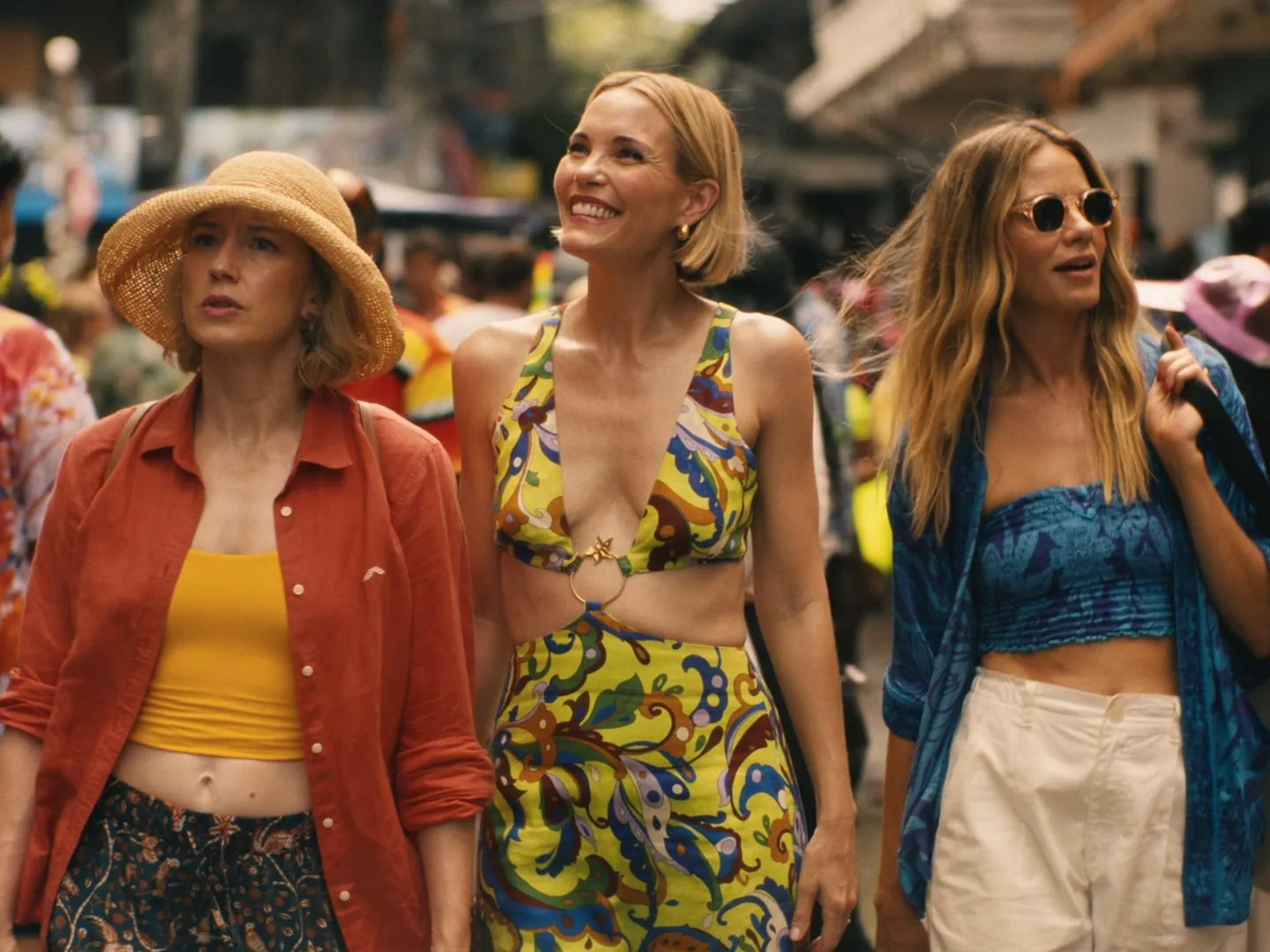Three women in colorful summer outfits walking through a bustling outdoor market
