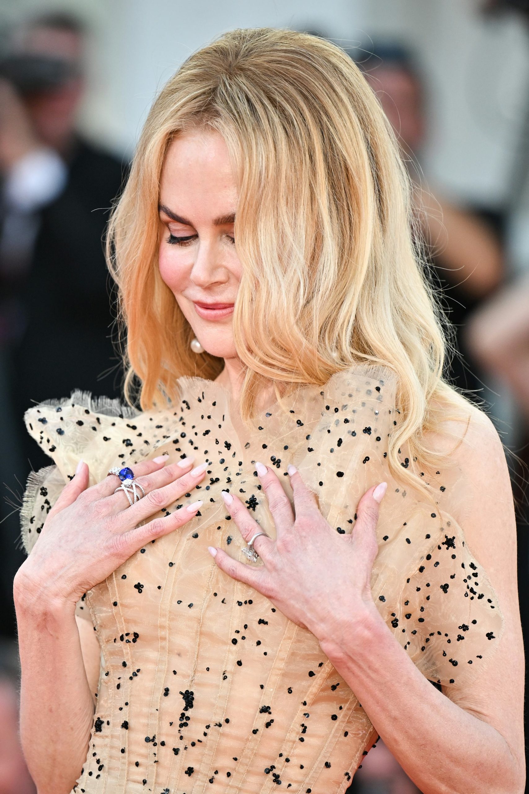 Woman with long blonde hair wearing a ruffled beige gown with black sequins at a formal event
