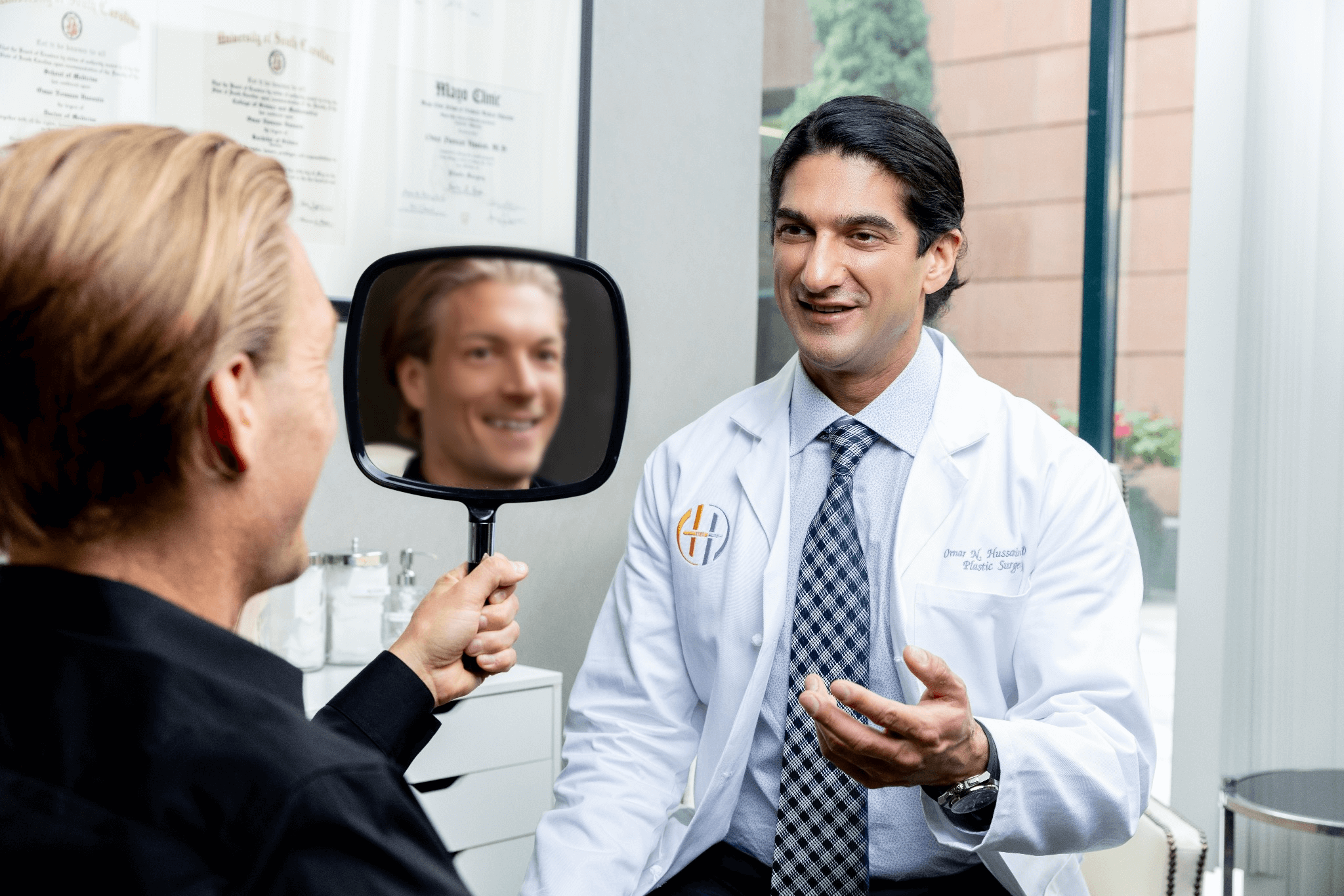 Patient reviews expected facelift results in a handheld mirror during consultation with the surgeon