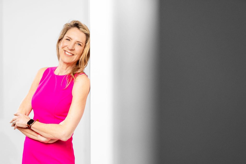 Plastic surgeon in a bright dress smiling, representing approachable care and guidance for patients considering breast implant revision or removal