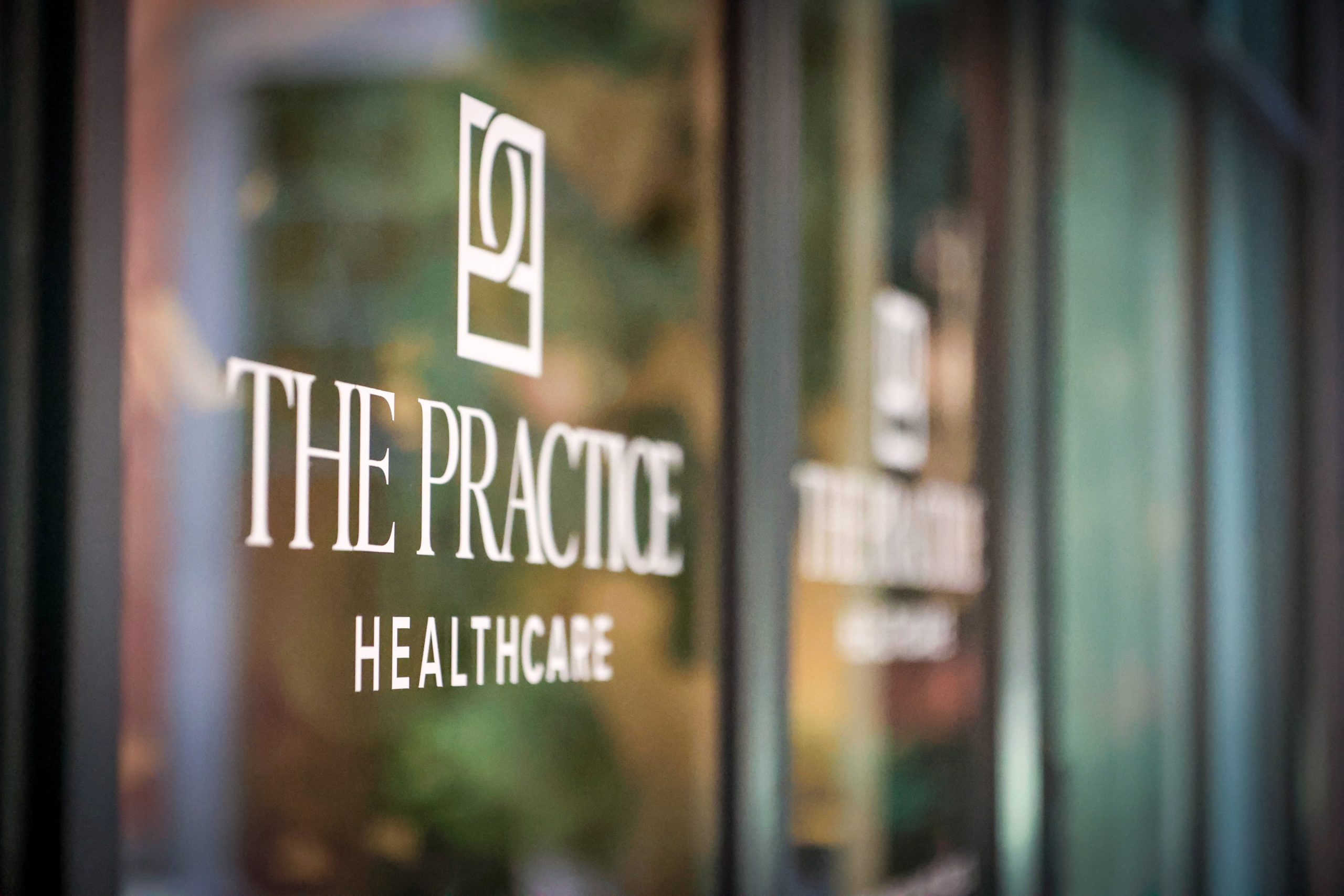 The Practice Healthcare logo signage on the glass entrance to the Beverly Hills breast reconstruction and integrated wellness facility