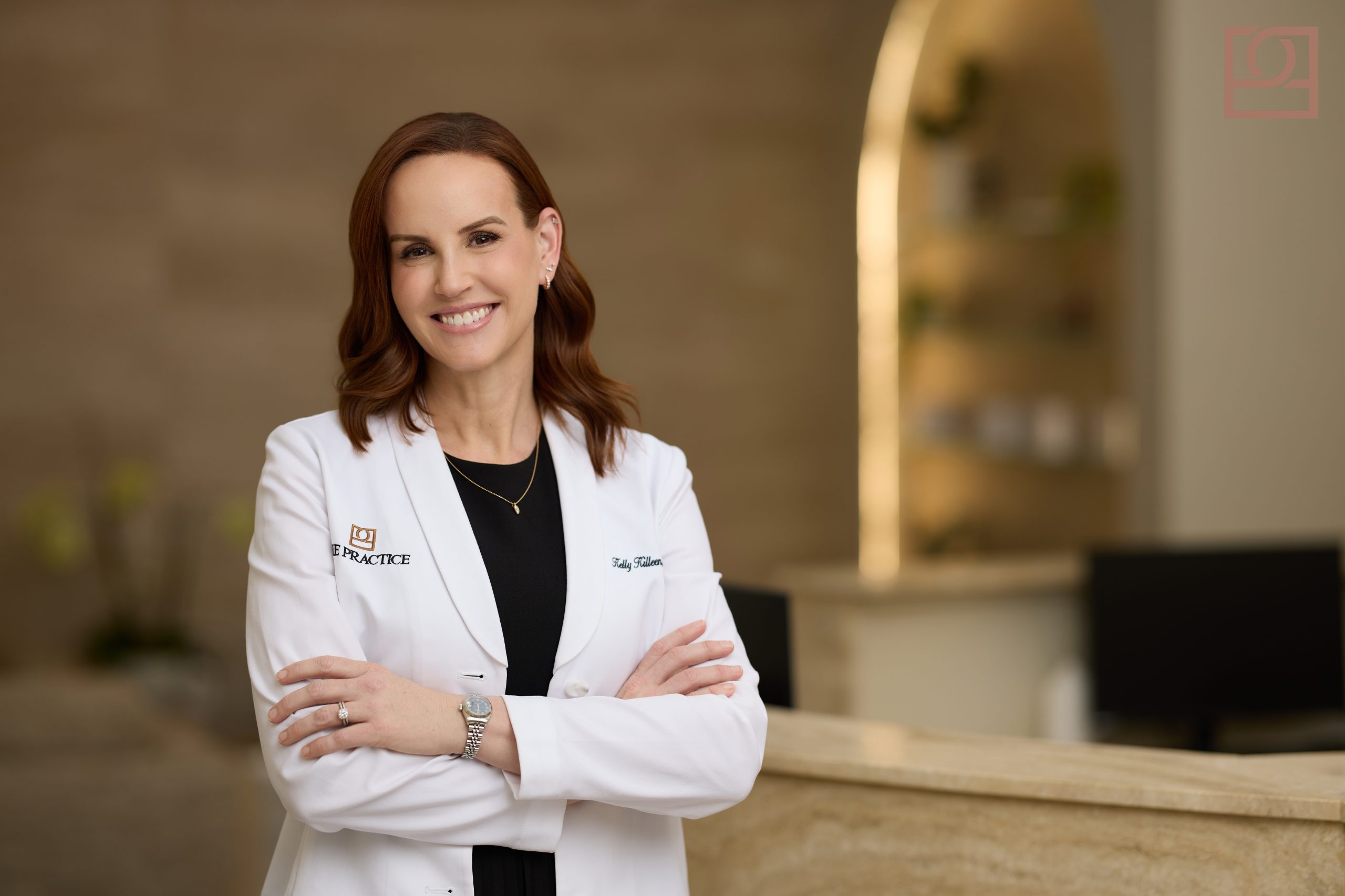 Dr. Kelly Killeen, MD FACS Dr. Kelly Killeen, double board-certified plastic surgeon at The Practice Healthcare, in a white coat with arms crossed